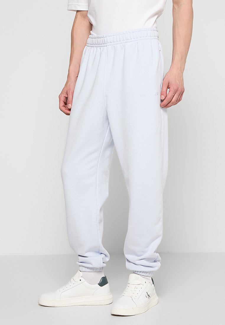 Helle blaue Jogginghose mit elastischem Bund, Seitentaschen, schmal zulaufenden Bündchen und dezentem Branding. Getragen mit weißen Sneakers.