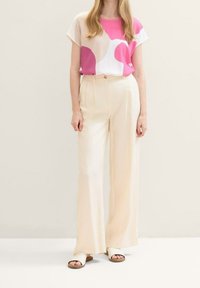 Outfit informale con una maglietta a strisce rosa e beige, pantaloni larghi color crema e sandali bianchi a scivolo, caratterizzati da un design rilassato e texture morbide.