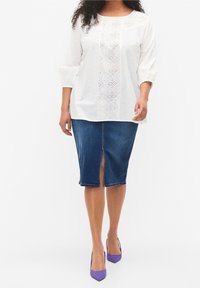 Hvid bluse med hulmønster detaljer, trekvartærmer; tætsiddende denimnederdel med frontslids; purpurfarvede høje hæle fuldender outfittet.
