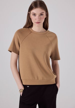 Short-sleeve, relaxed-fit top in light brown jersey fabric with a crew neckline and raglan sleeves. Subtle texture, minimal detailing.