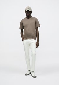 Καφέ βαμβακερό T-shirt, λευκό παντελόνι με ίσια πόδια και γκρι-άσπρα αθλητικά παπούτσια. Μια μπεζ καπέλο με ελαφρύ σχέδιο ολοκληρώνει το ντύσιμο.