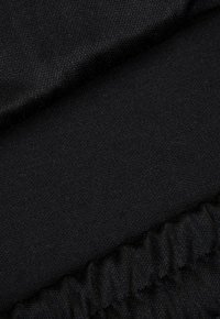 Czarna tkanina o gładkiej fakturze, z marszczonym fragmentem na dole. Materiał wydaje się miękki i elastyczny.