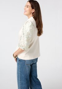 Lichtgekleurde blazer met elegante, gestructureerde mints groene mouwen. Het mouwontwerp heeft ingewikkelde patronen, gecombineerd met blauwe wijde jeans.