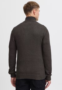Maglione lavorato a maglia di un grigio scuro con colletto alto, polsini e orlo a coste. Texture visibile e vestibilità rilassata, adatto all'abbigliamento casual.