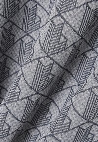 Tessuto grigio con motivo geometrico, caratterizzato da linee e trame blu navy, disposte in forme a freccia. Tessuto liscio e intrecciato.