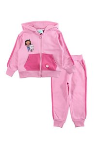 Survêtement deux pièces rose comprenant un sweat à capuche zippé avec poches, un motif graphique sur la poitrine, et un pantalon assorti à coupe fuselée avec des rayures latérales.