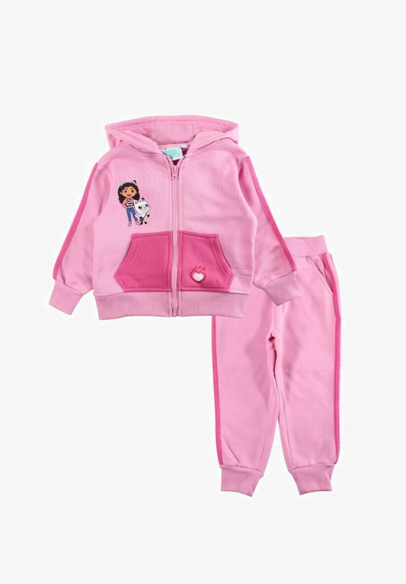 Survêtement deux pièces rose comprenant un sweat à capuche zippé avec poches, un motif graphique sur la poitrine, et un pantalon assorti à coupe fuselée avec des rayures latérales.