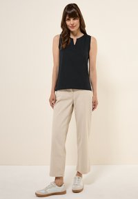 Top negro sin mangas con un escote tipo ojal, combinado con pantalones beiges holgados y zapatillas ligeras. Textura de tela simple y suave.