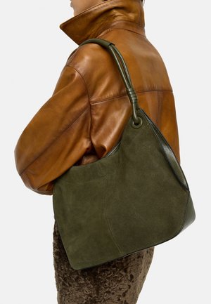 Osoba w brązowej skórzanej kurtce niesie dużą oliwkowo-zieloną torebkę zamszową z zaokrąglonym uchwytem na ramieniu.