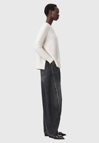 Maglione bianco a maglia con motivo testurizzato, abbinato a jeans neri a vita alta e gamba larga. Scarpe nere a punta con fibbie. Vista laterale.