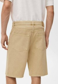 Khaki denim kratke hlače z dvema zadnjima žepekoma, pasom in šivi. Material ima teksturiran zaključek.