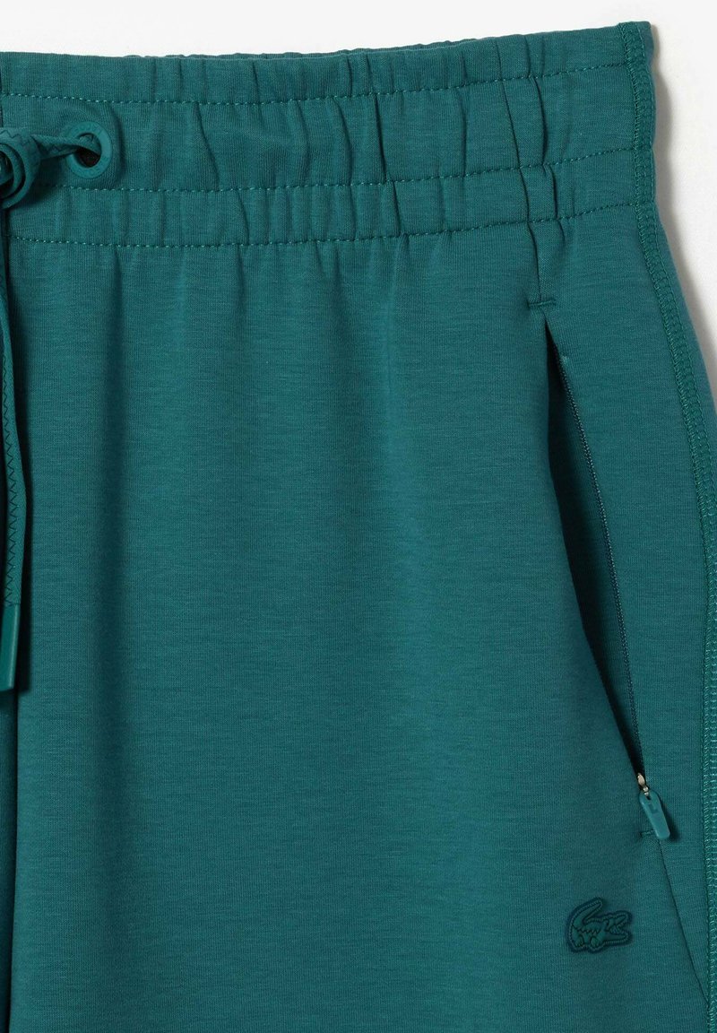 Turkusowe szorty dresowe z elastycznym pasem i sznurkiem do regulacji, z bocznymi kieszeniami na zamek oraz subtelnym logo na dolnej części nogawki.