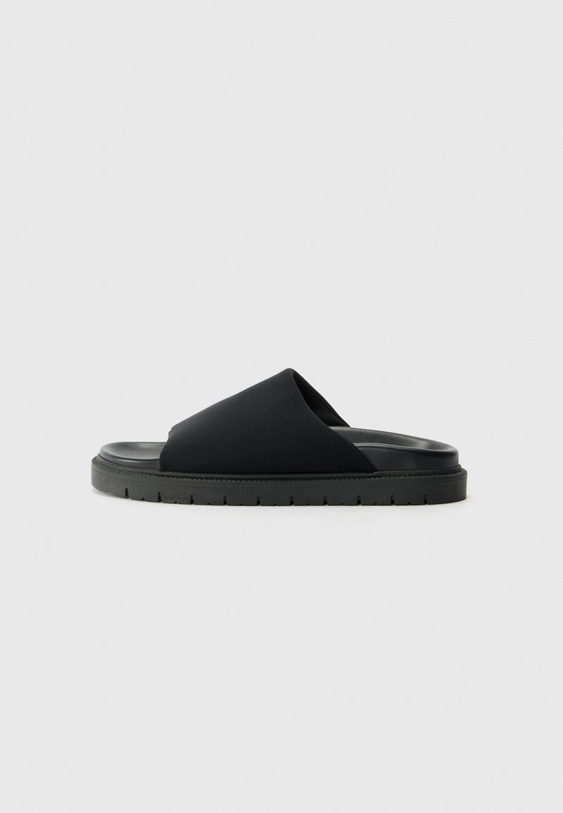 Svart glidesandal laget av mykt stoff med en bred rem over toppen og en tykk gummisåle med mønstrede spor.