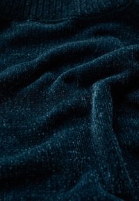 Texturerad, mörkblått tyg med ett ribbat mönster; mjuk pile; draperad i veck som framhäver dess plyschiga kvalitet och färgens djup.