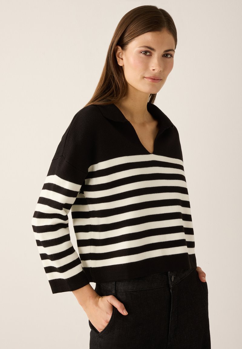 Zwart-wit gestreepte trui met een V-hals en kraag, gemaakt van geribbelde gebreide stof, gedragen met een zwarte spijkerbroek.
