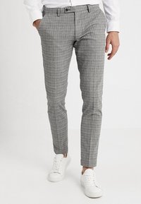 Šedé kostkované kalhoty slim fit s předními kapsami, poutky na opasek a plochým předním dílem, zakončené bílými teniskami.