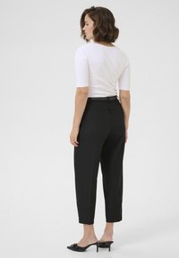 Black tailored trousers with a high waist, tapered legs, and front pleats, paired with a fitted white top and black heeled mules.