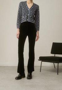 Pantalones de terciopelo negro acampanados combinados con un cárdigan de rayas en azul y gris que cuenta con un escote en V y cierre de botones, todo ello presentado sobre un fondo neutral.