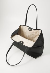 Svart läder tote-väska med öppen topp, utrustad med två handtag och en beige inredning. Inuti är det mönstrat med varumärket "GUESS."