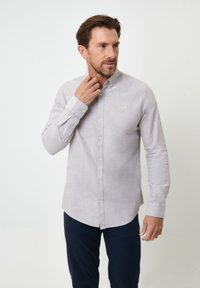 Camisa de botón de manga larga en gris claro con cuello clásico, que presenta una textura sutil y un pequeño logotipo bordado en el pecho.