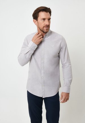Camisa de botón de manga larga en gris claro con cuello clásico, que presenta una textura sutil y un pequeño logotipo bordado en el pecho.