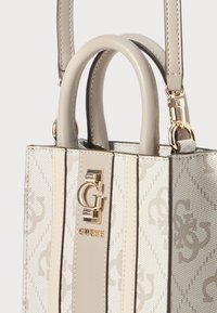 Beige og creme Guess håndtaske med monogram mønster, guld "G" logo detalje, to afrundede håndtag og en aftagelig skulderrem med guld hardware.