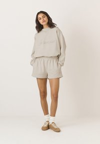 Beżowy sweatshirt z haftem "Matina", w połączeniu z pasującymi szortami. Miękka tkanina, luźny fason i ściągacze przy rękawach, zestawione z trampkami.