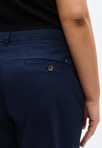 Βαμβακερό παντελόνι σε ναυτικό μπλε χρώμα με πίσω τσέπη που κλείνει με κουμπί και μικρή λογότυπη λεπτομέρεια κοντά στην τσέπη.