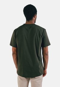 T-shirt en coton vert foncé avec des manches courtes et un col rond, présentant une texture lisse et une coupe décontractée. Aucune motif visible.