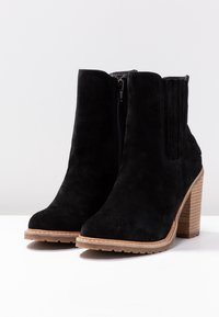 Botines de ante negros con un bloque de tacón marrón texturizado, cremallera lateral y paneles elásticos para un mejor ajuste. Punta redondeada y suela con relieve.