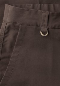 Pantalones de tela marrón oscuro que muestran la pretina, una trabilla con anillo metálico y detalles en la costura lateral.