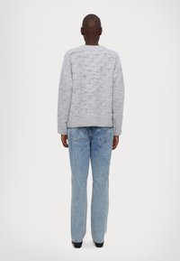 Γκρι πλεκτό πουλόβερ με υφασμάτινο μοτίβο, συνδυασμένο με ανοιχτό μπλε παντελόνι τζιν ίσιας γραμμής. Χωρίς ορατά ανάγλυφα ή διακοσμητικά στοιχεία.