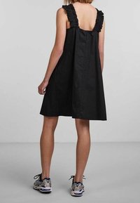 Svart ärmlös klänning med volangaxlar, A-linjedesign och enkel textur. Bärs med grå och blå träningsskor.