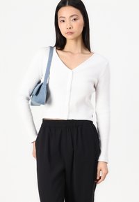 White ribbed cardigan with a V-neck, button closure, and long sleeves, paired with black elastic-waist trousers and a blue bag.