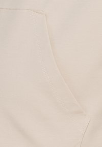 Detailní záběr béžové látky s viditelným šitím a kapsou na oděvu.