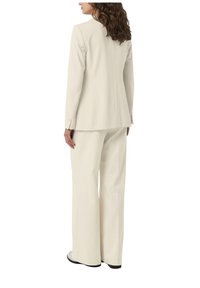 Kremowa, dopasowana blazer i pasujące szerokie spodnie, stukturalny design, gładka textura, minimalistyczny styl z akcentami guzików.