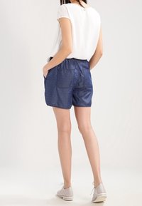 Tummansininen, pilkullinen shortsihame, jossa on joustava vyötärö ja sivutaskut, yhdistettynä valkoiseen yläosaan ja harmaisiin kenkiin.