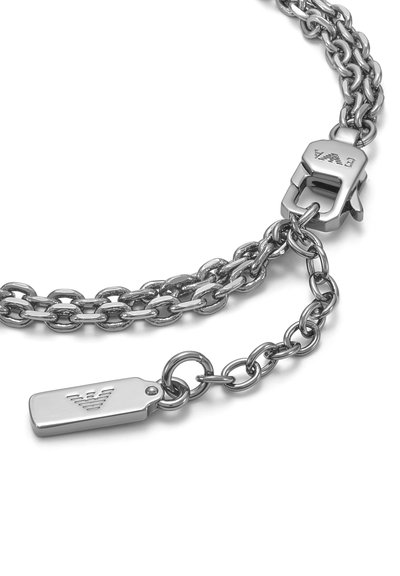 Bracelet à double chaîne en argent avec une étiquette rectangulaire présentant un logo gravé et un fermoir mousqueton gravé aux initiales de la marque.