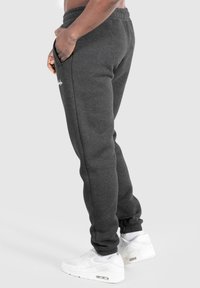 Graue Sporthosen mit einem gerippten Bund, seitlichen Taschen und umgekrempelten Knöcheln, kombiniert mit weißen Sportschuhen.