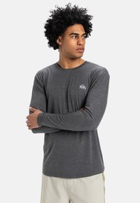 Långärmad grå T-shirt i lätt tyg, med en liten logotyp på vänster bröst, rund halsringning och figurnära design.