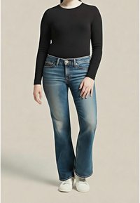 Haut à manches longues foncé assorti à un jean évasé bleu clair. Le jean présente un effet délavé sur les cuisses et un design classique à cinq poches. Chaussures blanches.