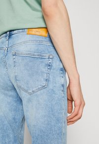 Lyseblå denimjeans med en lett falmet finish. Har en kontrasterende oransje lærlapp i livet og standard baklommer.