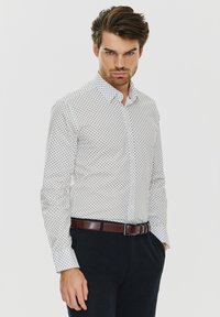 Biała koszula w małe granatowe kropki, z kołnierzykiem zapinanym na guziki, długimi rękawami i gładką teksturą, zestawiona z ciemnymi spodniami i brązowym paskiem.