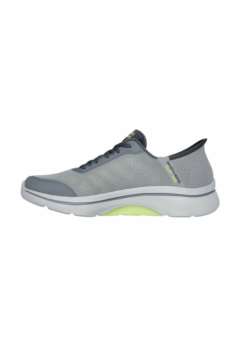 Zapatillas atléticas ligeras de malla gris con acentos verdes, con suela redondeada y diseño de cordones, adecuadas para caminar o uso casual.
