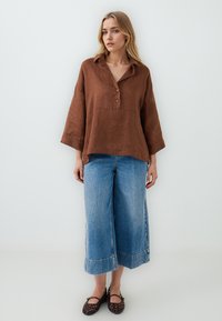 Top in lino marrone con colletto e tre bottoni, abbinato a ampie culotte in denim blu con orlo sfilacciato. Scarpe basse intrecciate marroni.
