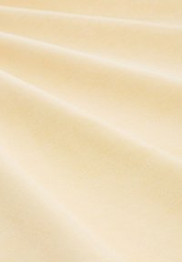 Tissu couleur crème présentant une surface lisse et texturée avec un éclat subtil et des plis diagonaux, reflétant doucement la lumière à travers le matériau.