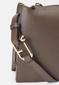 Bolsa de couro castanho com um design estruturado, apresentando um detalhe em metal dourado e uma superfície texturizada. Inclui uma alça ajustável.