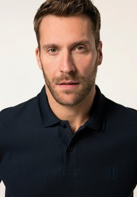 Námořnická polokošile s trojicí knoflíků, krátkými rukávy a decentním prošitím. Na levé části hrudníku je umístěno logo.