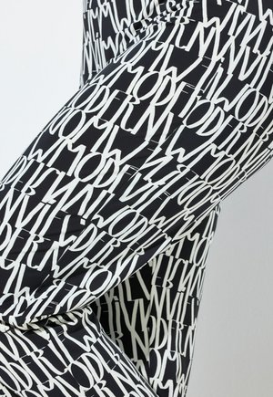 Schwarze Leggings mit einem durchgehenden weißen Textmuster, auf dem das Wort "MODERN" in verschiedenen Ausrichtungen abgebildet ist. Glatter, eng anliegender Stoff.