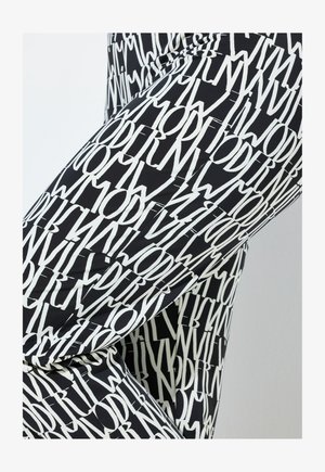 Zwarte legging met een wit all-over tekstpatroon waarin het woord "MODERN" in verschillende richtingen staat. Soepele, aansluitende stof.